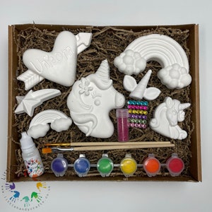 May include: A unicorn craft kit with white ceramic pieces, paint, brushes, and glitter. The kit includes a unicorn head, a heart with the word "Unicorn" on it, a rainbow, a star, and two smaller unicorn figures.