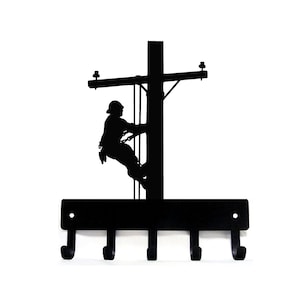 May include: Black metal key holder shaped like a silhouette of a lineman climbing a utility pole. The key holder has five hooks.