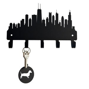 May include: Black metal key holder shaped like the Chicago skyline with five hooks. A silver key with a dachshund silhouette charm is hanging from one of the hooks.