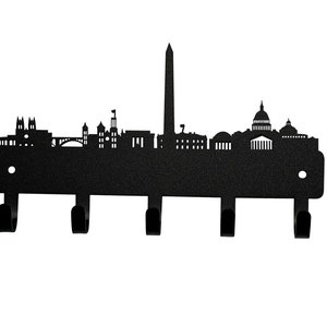 May include: Black metal key rack shaped like the Washington D.C. skyline. The rack has five hooks and features iconic landmarks like the Washington Monument, the Capitol Building, and the White House.