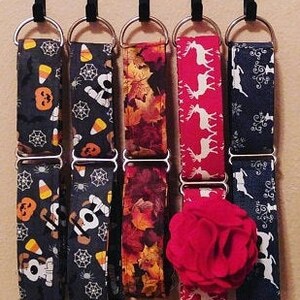 K&ouml;nnte beinhalten: F&uuml;nf verschiedene gemusterte Hundehalsb&auml;nder h&auml;ngen an einem schwarzen Metallgestell. Die Halsb&auml;nder sind aus Stoff und haben verschiedene Designs, darunter Mais, Spinnen, Bl&auml;tter, Rentiere und ein Schneeflockenmuster.