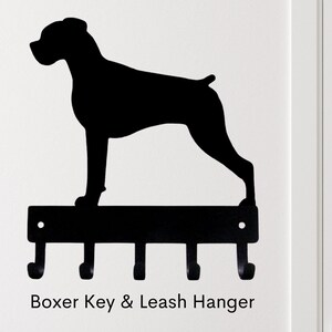 May include: Black metal key and leash hanger shaped like a Boxer dog silhouette. The hanger has four hooks and the text "Boxer Key & Leash Hanger" is printed below.