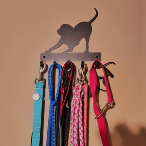 Black powder coated, five hook, key rack with the silhouette of a dog bowed in a playful stance with it's hind quarters and tail in the air. The rack is mounted on a tan wall and the hooks of the key rack hold multiple dog leashes.