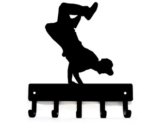May include: Black metal key holder with a silhouette of a person doing a handstand. The key holder has five hooks.