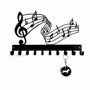 May include: Black metal key holder featuring musical notes and a treble clef design. The key holder has eight hooks and includes a round keychain with a dachshund silhouette.