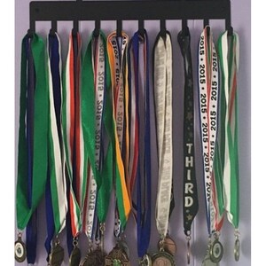 May include: A black metal medal display rack with 10 medals hanging on it. The medals are various colors, including green, white, red, orange, yellow, and black. The medals have different designs and text, including "SOIP" and "THIRD".