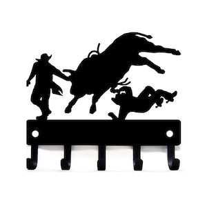Black powder coated, five hook, metal key rack with a silhouette of a rodeo scene of a bullrider falling from a bucking bull, a rodeo clown is in front with it's arm out to the bull.