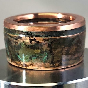 May include: A copper ring with a green and brown patina finish. The ring has a wide band and a smooth, polished surface.