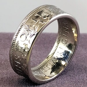 May include: A silver ring made from a repurposed Canadian one dollar coin. The ring features the inscription "ONE DOLLAR" and "CANADA" on the outside of the band. The inside of the band features a thistle design.