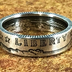 May include: Silver ring made from a US half dollar coin. The ring features the words "LIBERTY" and two stars on the side.