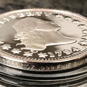 Puede incluir: Primer plano de una moneda de plata de 1794 con el perfil de una mujer y la palabra "LIBERTY". La moneda est&aacute; marcada con "1 TROY OZ. .999 FINE SILVER".
