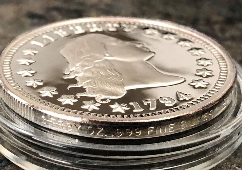 Puede incluir: Primer plano de una moneda de plata de 1794 con el perfil de una mujer y la palabra "LIBERTY". La moneda est&aacute; marcada con "1 TROY OZ. .999 FINE SILVER".