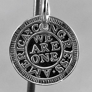 May include: Silver charm with the words "We Are One" inside a circle and "African Congress" around the outside.