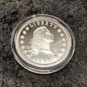Puede incluir: Una moneda de plata dentro de un estuche de pl&aacute;stico transparente. La moneda muestra el perfil de una mujer, la palabra "LIBERTY", estrellas y el a&ntilde;o "1794". Una pieza de colecci&oacute;n hist&oacute;rica.
