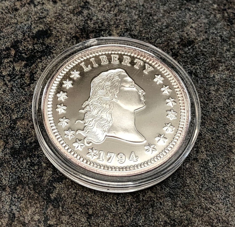 Puede incluir: Una moneda de plata dentro de un estuche de pl&aacute;stico transparente. La moneda muestra el perfil de una mujer, la palabra "LIBERTY", estrellas y el a&ntilde;o "1794". Una pieza de colecci&oacute;n hist&oacute;rica.