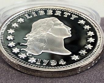May include: A silver coin with a black background featuring a profile of a woman, the word "LIBERTY", and the year "1794". The coin has a detailed edge and is surrounded by stars.