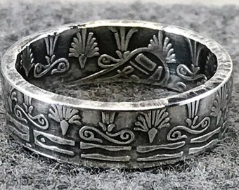 May include: A silver ring made from a coin with an intricate design of stylized flowers and swirls.