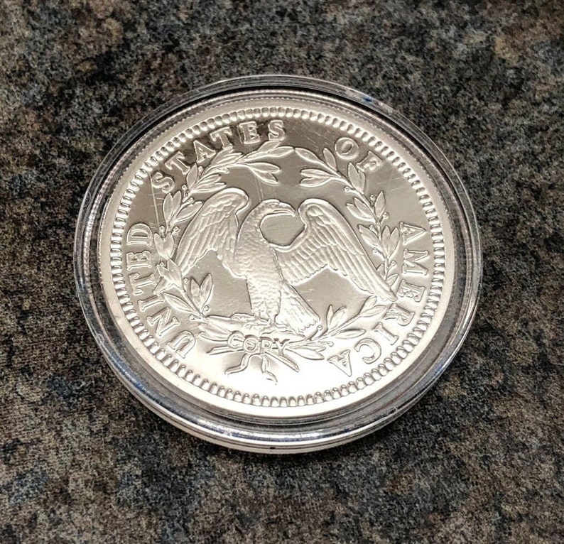 Puede incluir: Una moneda plateada con un &aacute;guila y la inscripci&oacute;n "UNITED STATES OF AMERICA". La moneda est&aacute; dentro de un estuche de pl&aacute;stico transparente. La palabra "COPY" tambi&eacute;n es visible.