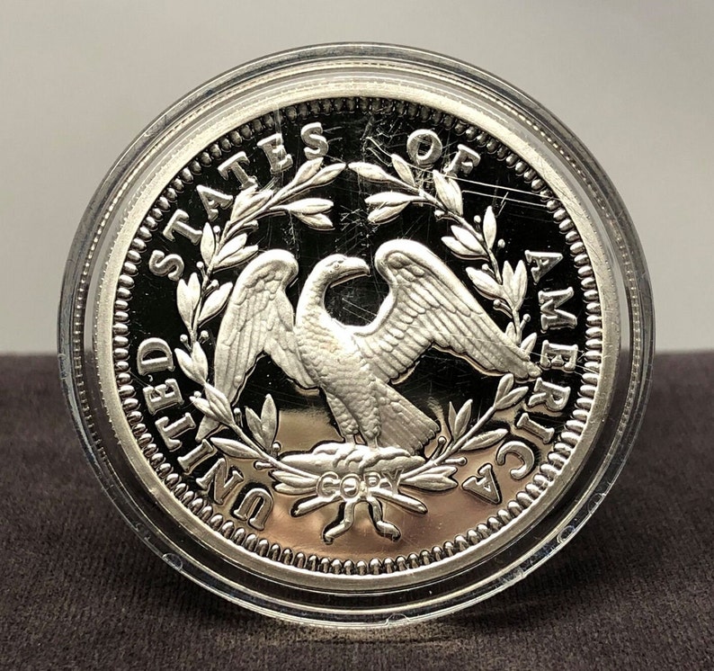 Puede incluir: Una moneda de plata con un &aacute;guila con las alas extendidas, rodeada por la inscripci&oacute;n "UNITED STATES OF AMERICA". La moneda est&aacute; dentro de una funda protectora transparente. La palabra "COPY" es visible.