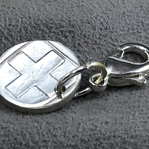 May include: Silver keychain with a round charm featuring a white cross on a silver background. The charm is attached to a silver lobster clasp.