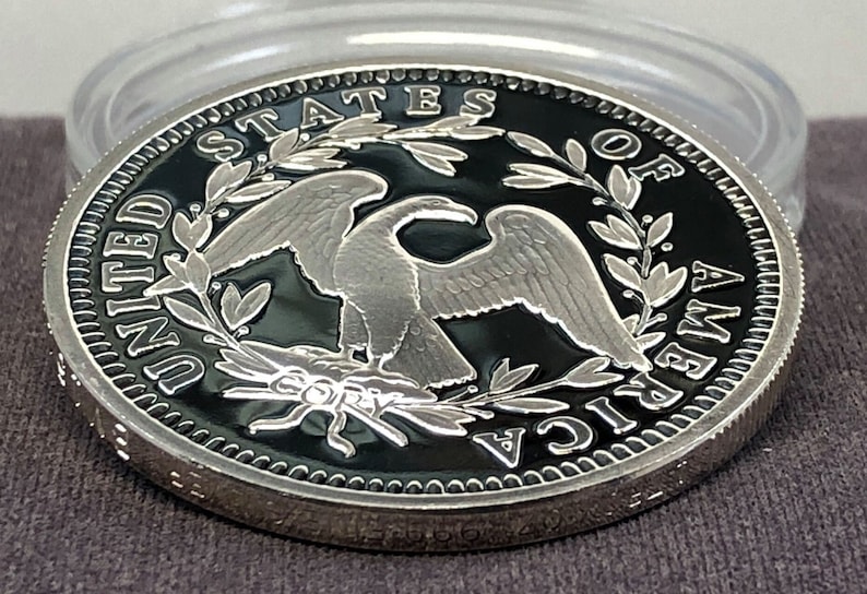 Puede incluir: Una moneda de plata con fondo negro, con un dise&ntilde;o de &aacute;guila y las palabras "UNITED STATES OF AMERICA". La moneda est&aacute; en una funda de pl&aacute;stico transparente. La palabra "COPY" es visible.