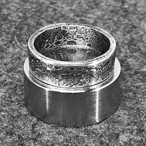 May include: Two silver rings stacked on top of each other. The top ring has a textured finish, while the bottom ring has a smooth finish.