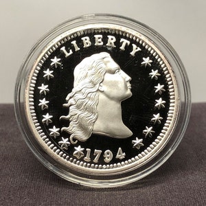 Puede incluir: Una moneda de plata con el perfil de una mujer, la palabra "LIBERTY" arriba y la fecha "1794" abajo. La moneda est&aacute; dentro de un estuche transparente. El borde de la moneda est&aacute; decorado con estrellas.