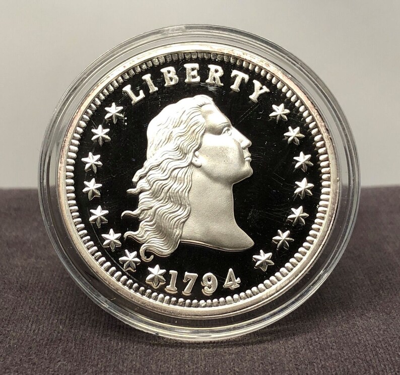 Puede incluir: Una moneda de plata con el perfil de una mujer, la palabra "LIBERTY" arriba y la fecha "1794" abajo. La moneda est&aacute; dentro de un estuche transparente. El borde de la moneda est&aacute; decorado con estrellas.