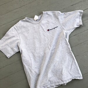 May include: A gray short-sleeved t-shirt with a small embroidered Champion logo in black and red.
