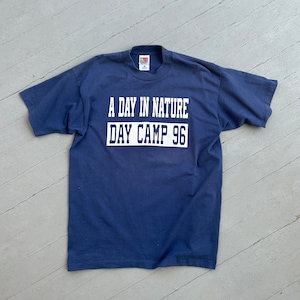 May include: A navy blue t-shirt with white text that reads "A Day in Nature Day Camp 96".