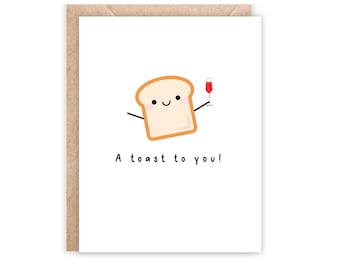 May include: A greeting card with a cartoon illustration of a slice of bread holding a glass of red wine. The text "A toast to you!" is written below the illustration. The card has a white background and a brown border.