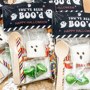 May include: Halloween-themed gift bags with the text "You've Been BOO'd Happy Halloween!" Each bag contains a ghost-shaped marshmallow, hot cocoa mix, candy, a wooden spoon, and a striped candy cane.