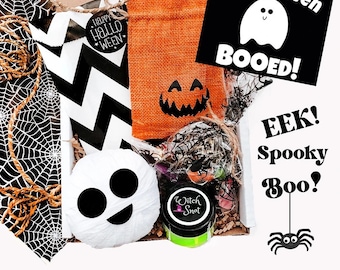 May include: A Halloween-themed gift box filled with various items. Includes a white ghost-shaped decoration, an orange burlap bag with a jack-o'-lantern face, and a black and white chevron patterned bag. The box also contains a jar of green slime and a sign that says "You've been BOOED!"