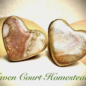May include: Two heart-shaped objects with a marbled appearance, featuring shades of brown, gold, and white. The objects are set against a soft, blurred background. The text "Haven Court Homestead" is at the bottom.