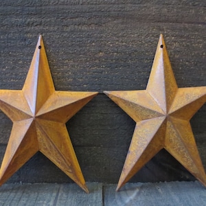 May include: Two rustic, five-pointed, metal stars with a distressed, rusty finish. The stars are a warm, golden brown color and have a hole at the top for hanging.