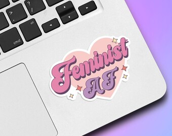 May include: A pink heart-shaped sticker with the text "Feminist AF" in a retro font. The sticker is on a silver laptop.