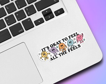 May include: A white laptop with a sticker that says "It's okay to feel all the feels." The sticker features five colorful cartoon faces with different expressions.