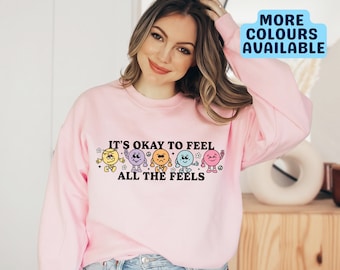 May include: Pink sweatshirt with the text "It's okay to feel all the feels" and a row of five colorful cartoon faces with different expressions.