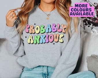 Puede incluir: Una sudadera gris con el texto "Probably Anxious" en letras de colores arcoíris. Las letras están en una fuente retro, con forma de burbuja.