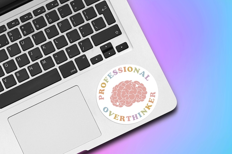 May include: A round sticker with the words "PROFESSIONAL OVERTHINKER" in pastel colors encircling a pink brain graphic. The sticker is placed on a silver laptop keyboard against a gradient background of purple and blue.