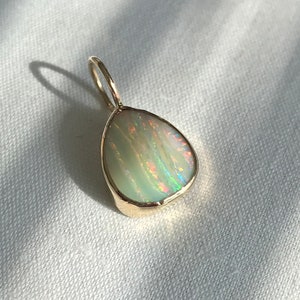 May include: A gold pendant featuring a white opal with iridescent rainbow flashes. The opal is set in a smooth, rounded shape.