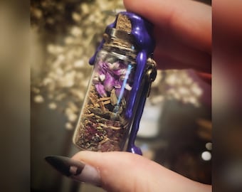 May include: A small glass bottle filled with dried herbs and purple flowers, sealed with a cork and purple wax. The bottle's contents are visible through the clear glass, showcasing the natural elements within. The wax drips down the sides, adding a decorative touch.