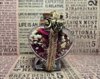 Può includere: Una bottiglia di vetro a forma di cuore piena di fiori ed erbe essiccate. La bottiglia è adornata da un tappo di sughero, spago e un ciondolo a forma di luna crescente e stella color bronzo. Lo sfondo presenta un collage di testo.