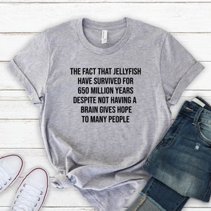 May include: A gray t-shirt with the text "THE FACT THAT JELLYFISH HAVE SURVIVED FOR 650 MILLION YEARS DESPITE NOT HAVING A BRAIN GIVES HOPE TO MANY PEOPLE" printed in black.