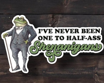 May include: A die-cut sticker featuring an illustration of a frog dressed in a formal grey suit, white shirt, and bow tie, holding a walking cane. The text reads, I'VE NEVER BEEN ONE TO HALF-ASS SHENANIGANS, with the word Shenanigans in green.
