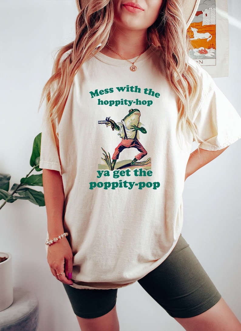 May include: A white t-shirt with a green frog graphic and the text "Mess with the hoppity-hop ya get the poppity-pop".