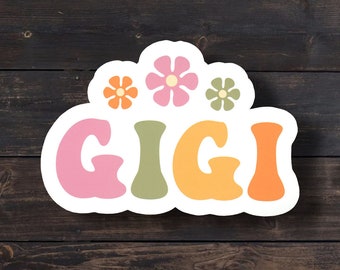 May include: A die-cut sticker featuring the name GIGI in large, rounded, colorful letters. The letters are pink, sage green, yellow, and orange. Above the name are three small, simple flower shapes in orange, pink, and sage green colors.