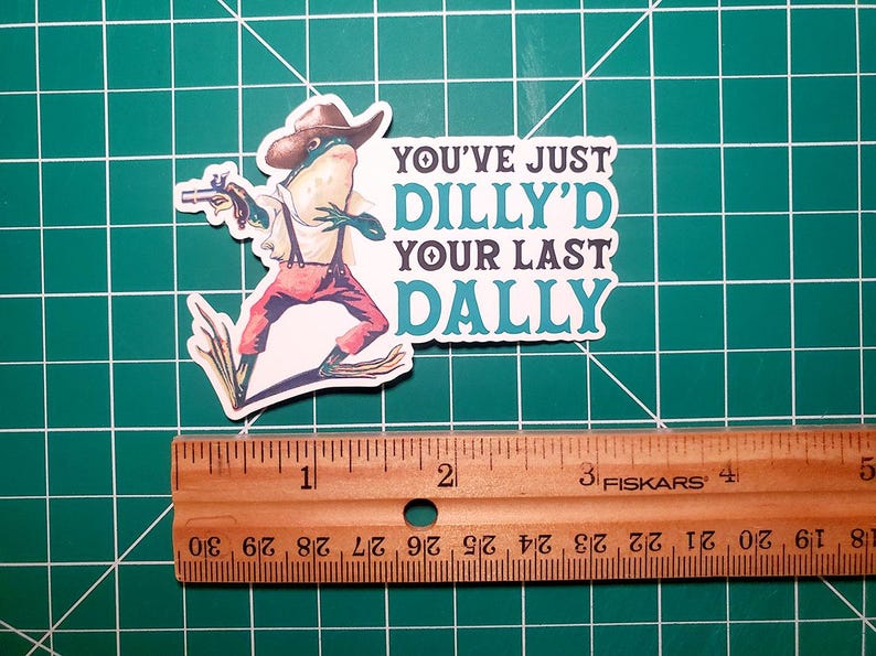 May include: A sticker featuring a cartoon frog wearing a cowboy hat and holding a gun. The text on the sticker reads "You've Just Dilly'd Your Last Dally."