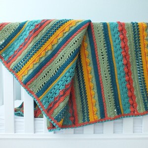 Puede incluir: Una manta de bebé de crochet colorida con rayas de color turquesa, verde, naranja y amarillo. La manta tiene un borde de crochet.