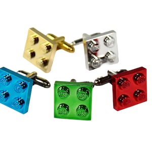 May include: Five cufflinks in the style of toy building blocks. The cufflinks are in gold, silver, blue, green, and red. Each cufflink has four raised circular studs and a silver post.